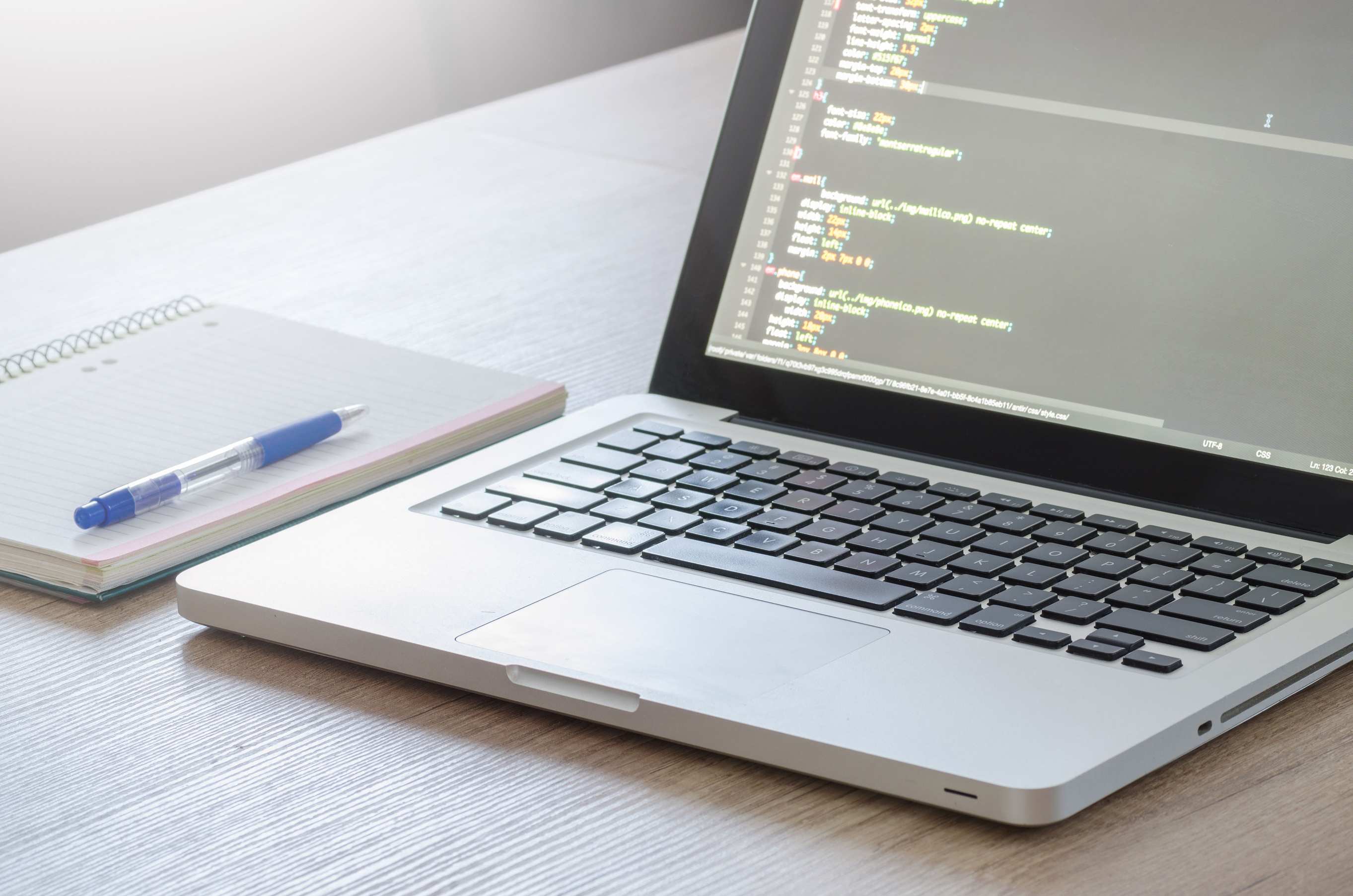Weit aufgenommener Arbeitsplatz mit Laptop und Monitor, Laptop mit Code-Editor auf Holzschreibtisch